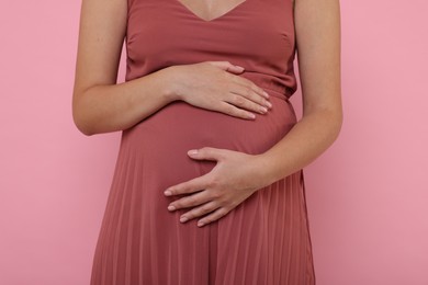 Photo of Pregnant woman in dress on pink background, closeup