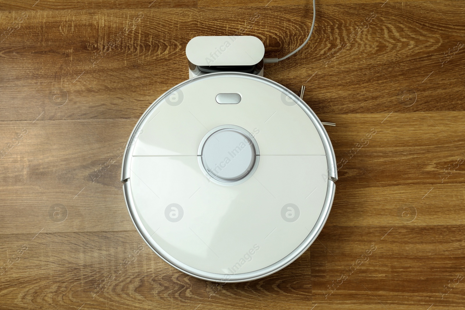 Photo of Robotic vacuum cleaner charging on wooden floor, top view