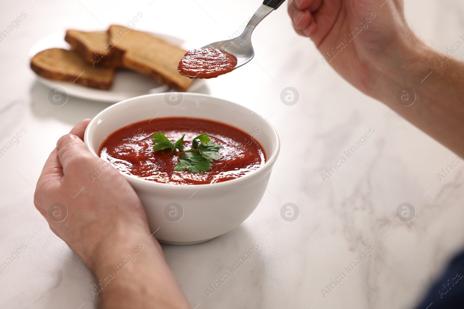 Photo of Man eating delicious tomato soup at light marble table, closeup