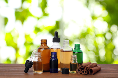 Bottles of essential oils and cinnamon sticks on wooden table against blurred background