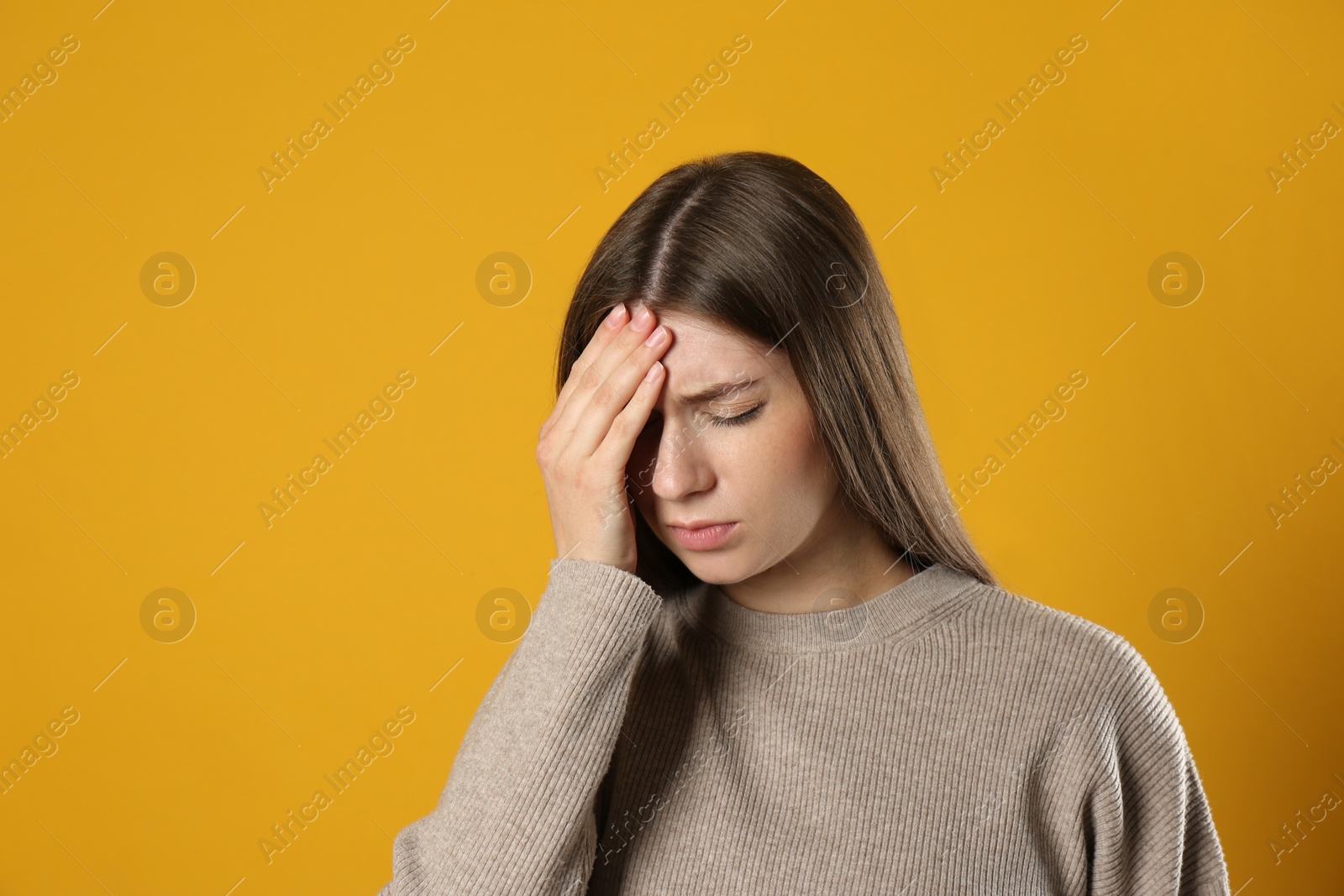 Photo of Young woman suffering from migraine on yellow background