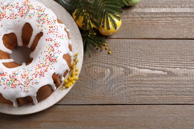 Glazed Easter cake with sprinkles, painted eggs and flowers on wooden table, flat lay. Space for text