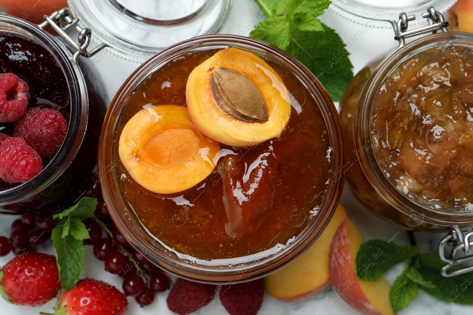 Photo of Jars with different jams and fresh fruits on white table, flat lay