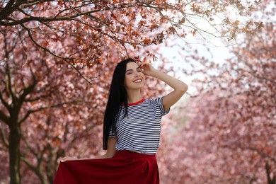 Photo of Pretty young woman wearing trendy clothes near beautiful blossoming trees outdoors. Stylish spring look