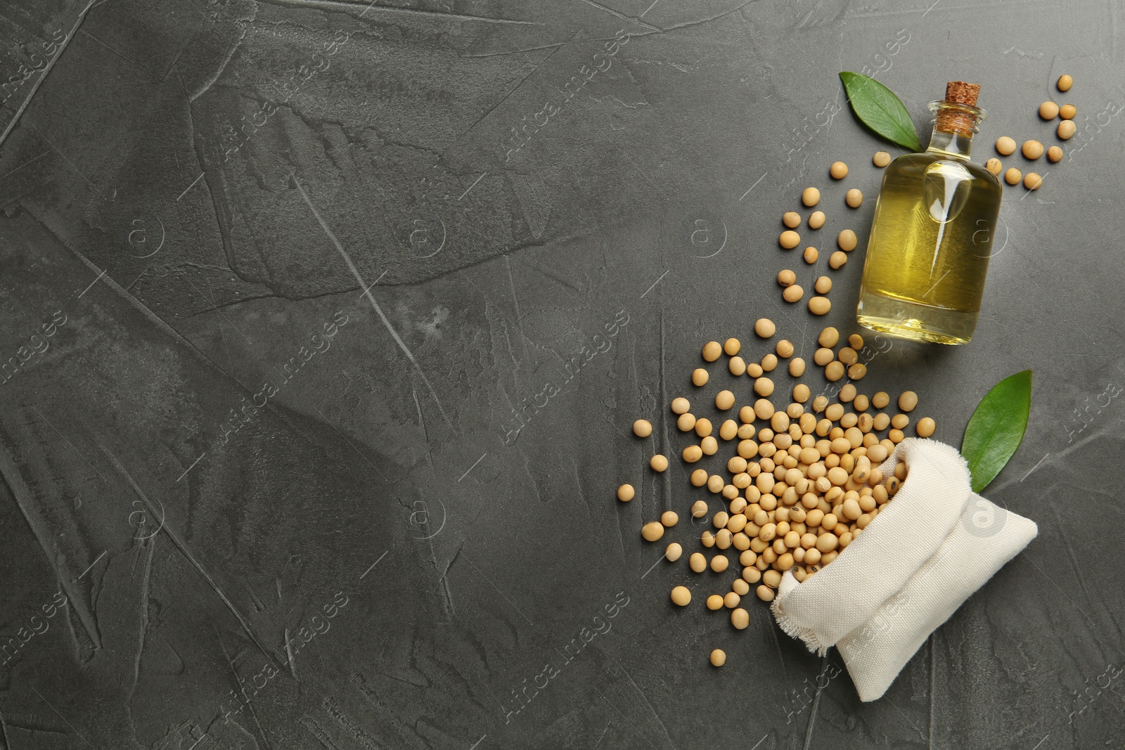 Photo of Glass bottle of oil, leaves and soybeans on grey table, flat lay. Space for text
