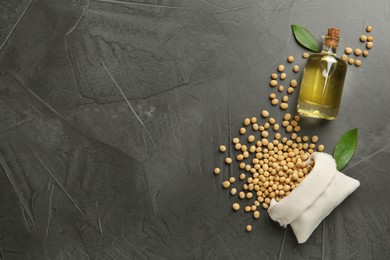 Glass bottle of oil, leaves and soybeans on grey table, flat lay. Space for text