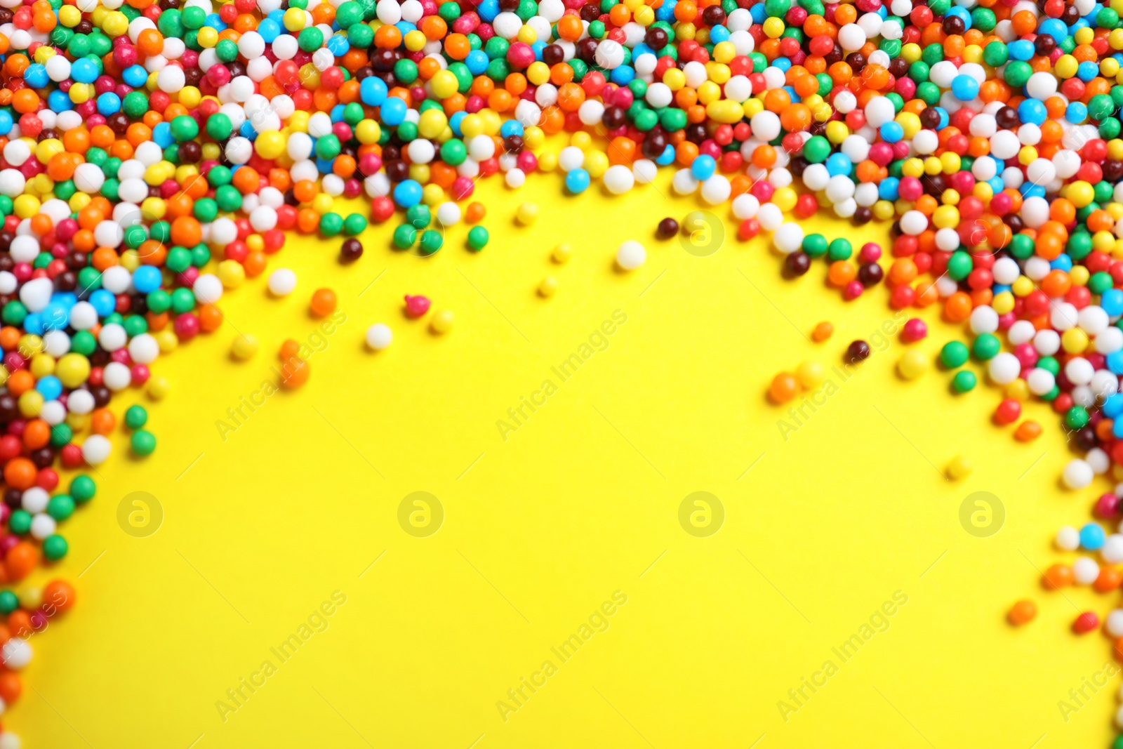 Photo of Bright colorful sprinkles on yellow background, flat lay with space for text. Confectionery decor