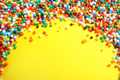 Photo of Bright colorful sprinkles on yellow background, flat lay with space for text. Confectionery decor