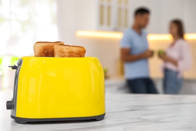 Photo of Modern toaster with slices of bread and blurred couple on background