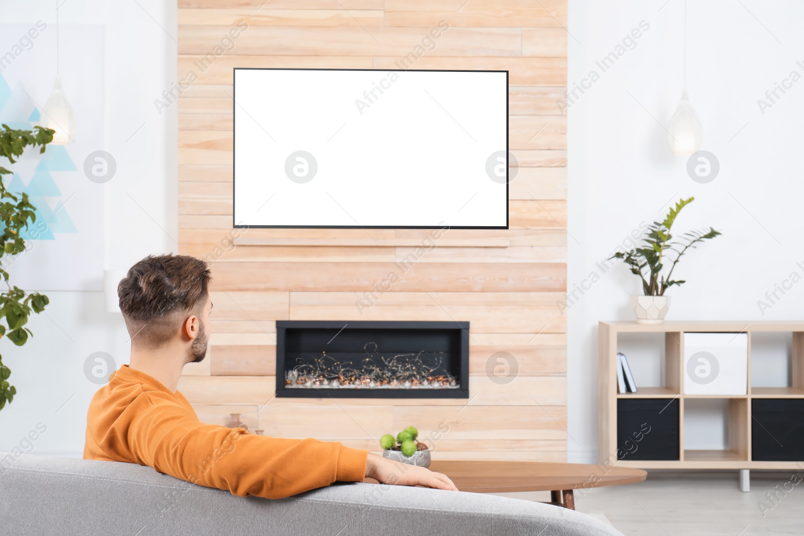 Photo of Man watching TV on sofa in living room with decorative fireplace