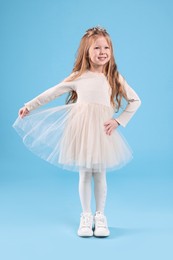 Photo of Cute girl in beautiful dress with diadem on light blue background. Little princess