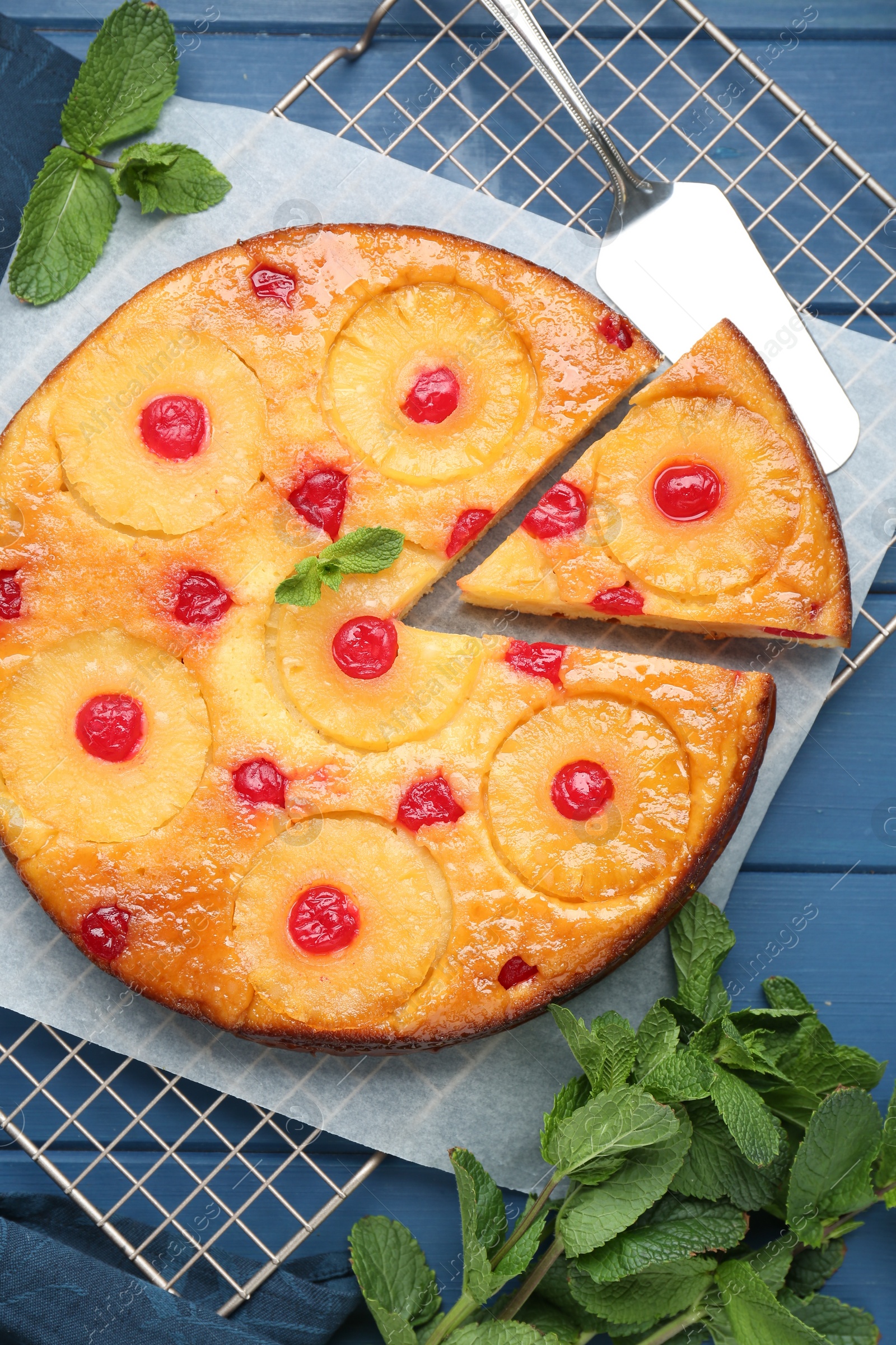 Photo of Delicious cut pineapple pie with cherry and mint on blue wooden table, flat lay