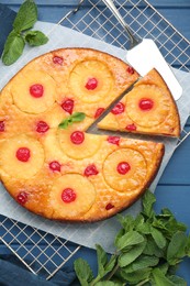 Photo of Delicious cut pineapple pie with cherry and mint on blue wooden table, flat lay