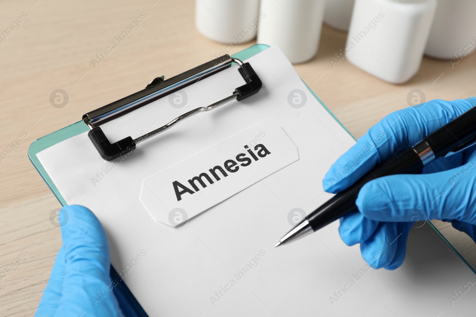 Photo of Doctor holding clipboard with word Amnesia at wooden table, closeup