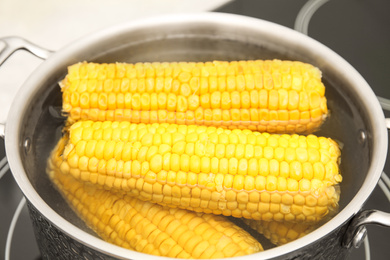 Photo of Pot with boiling fresh corn on cooktop, closeup