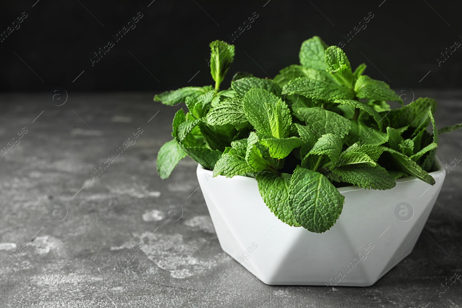 Photo of Bowl full of fresh green mint on grey table, space for text