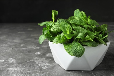 Bowl full of fresh green mint on grey table, space for text