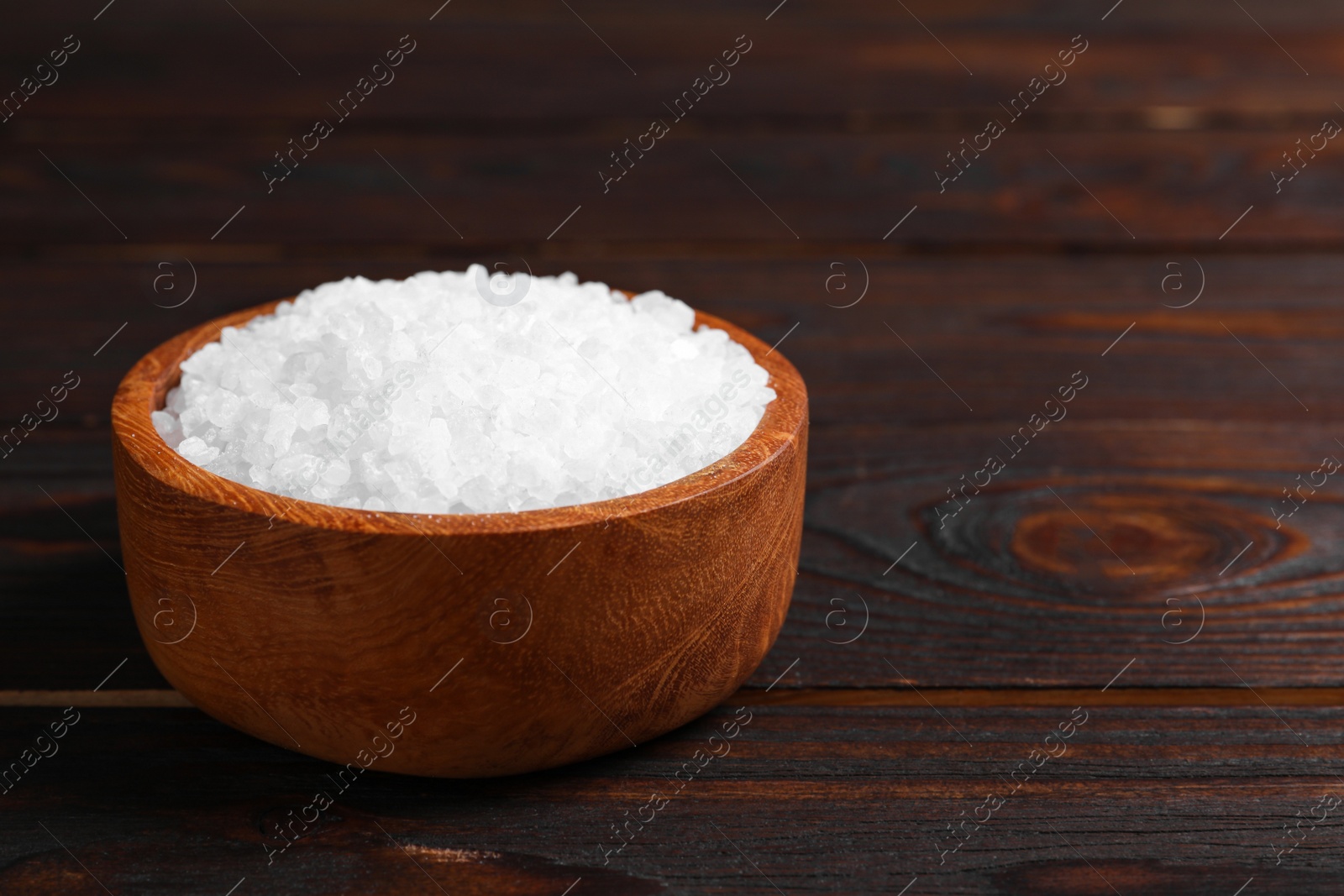 Photo of Bowl with natural sea salt on wooden table. Space for text