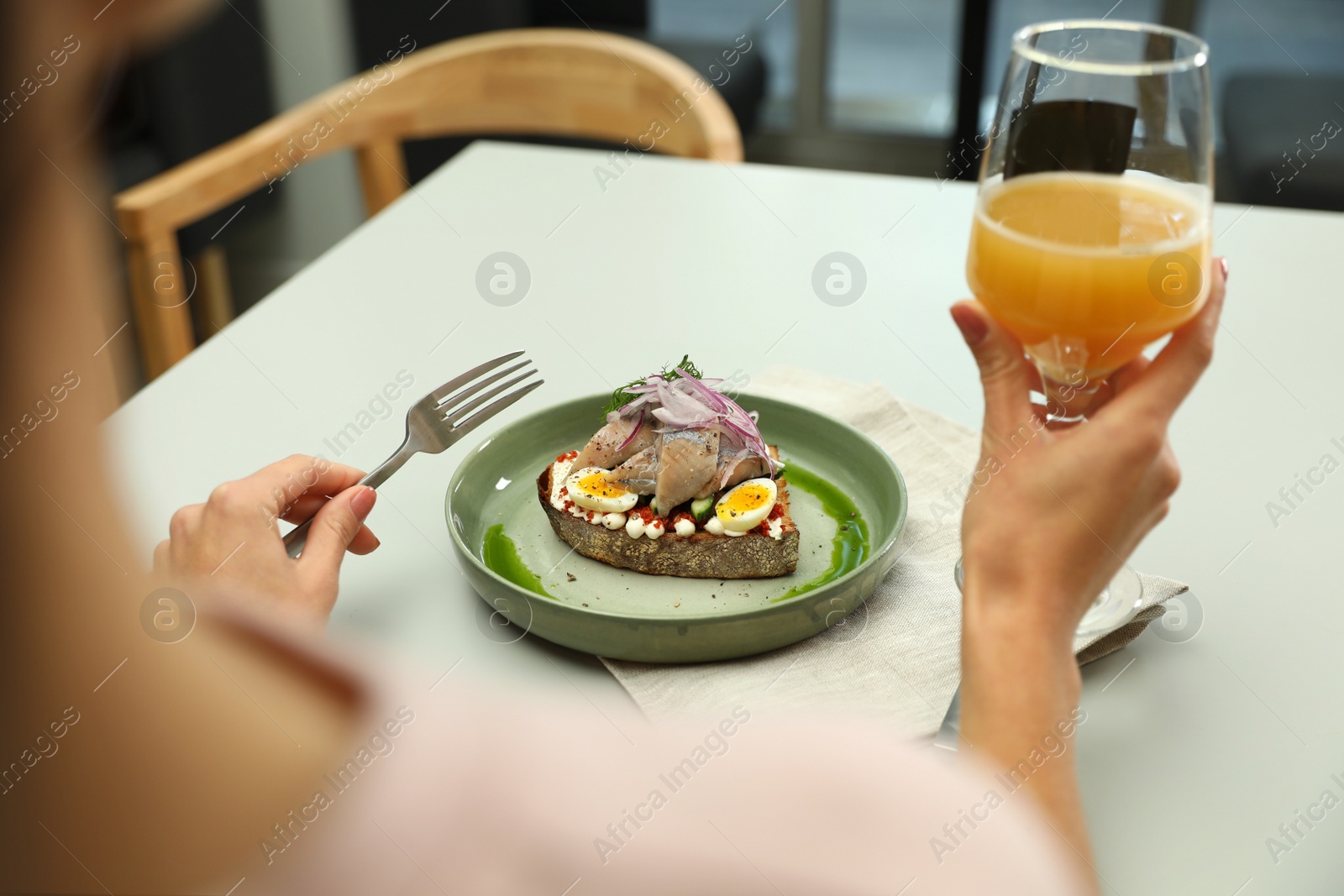 Photo of Woman with glass of beer and tasty fish sandwich at light table, closeup