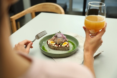 Woman with glass of beer and tasty fish sandwich at light table, closeup