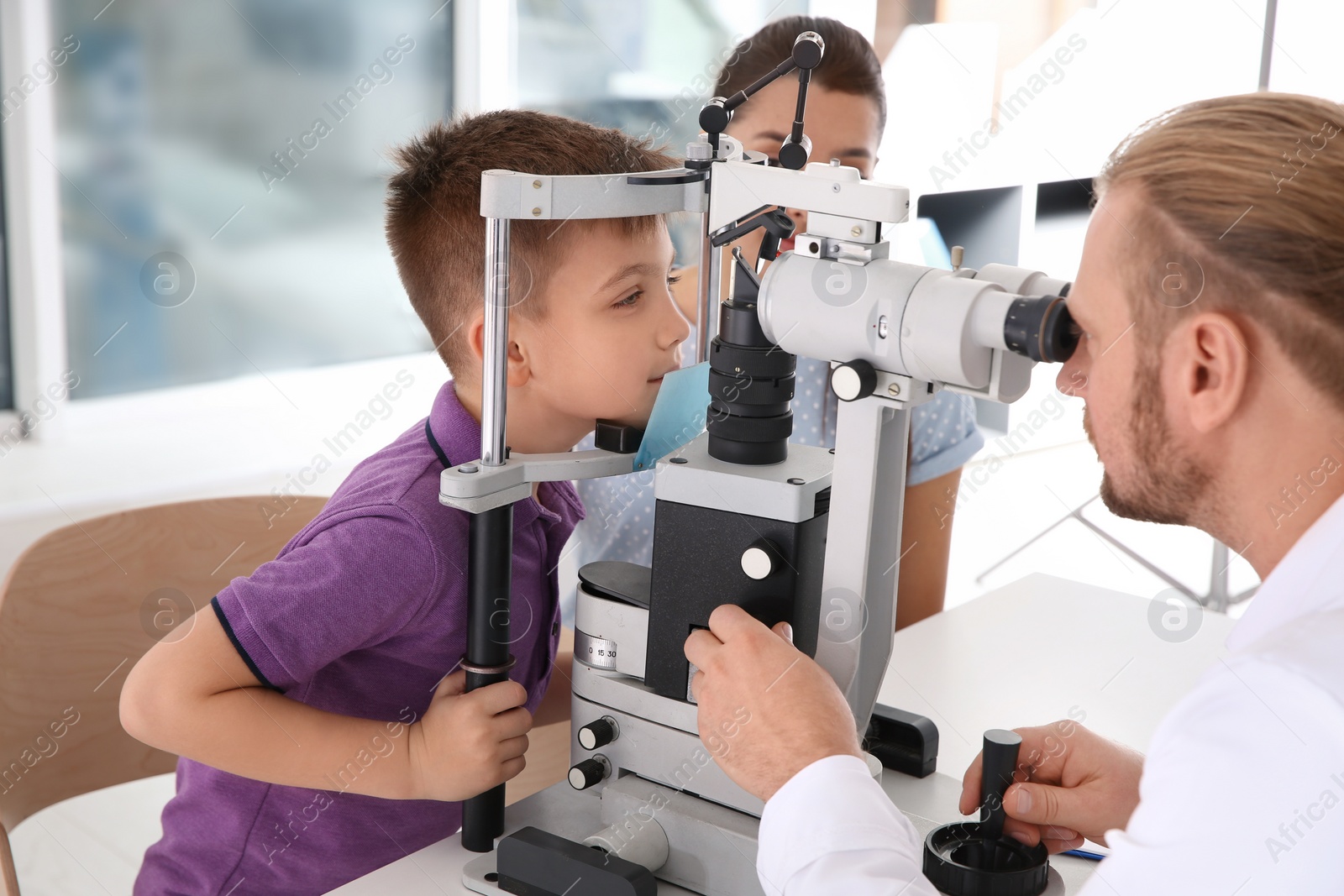 Photo of Children's doctor examining little boy with slit lamp in clinic