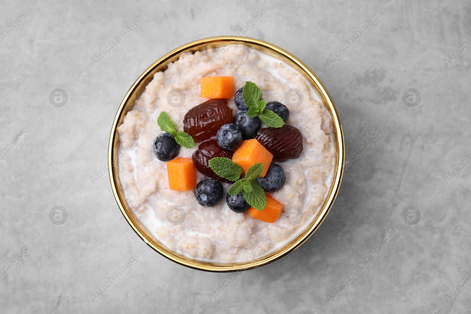 Photo of Delicious barley porridge with blueberries, pumpkin, dates and mint in bowl on grey table, top view
