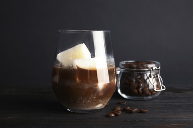 Coffee drink with milk ice cubes and beans on table against dark background