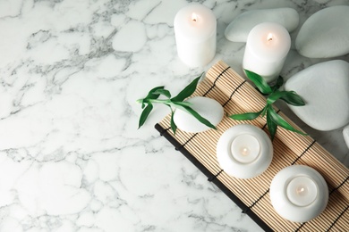 Beautiful spa composition with candles and bamboo mat on marble background, top view. Space for text