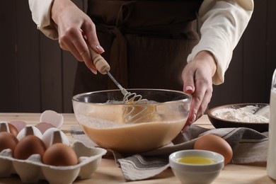 Woman making dough with whisk in bowl at table, closeup