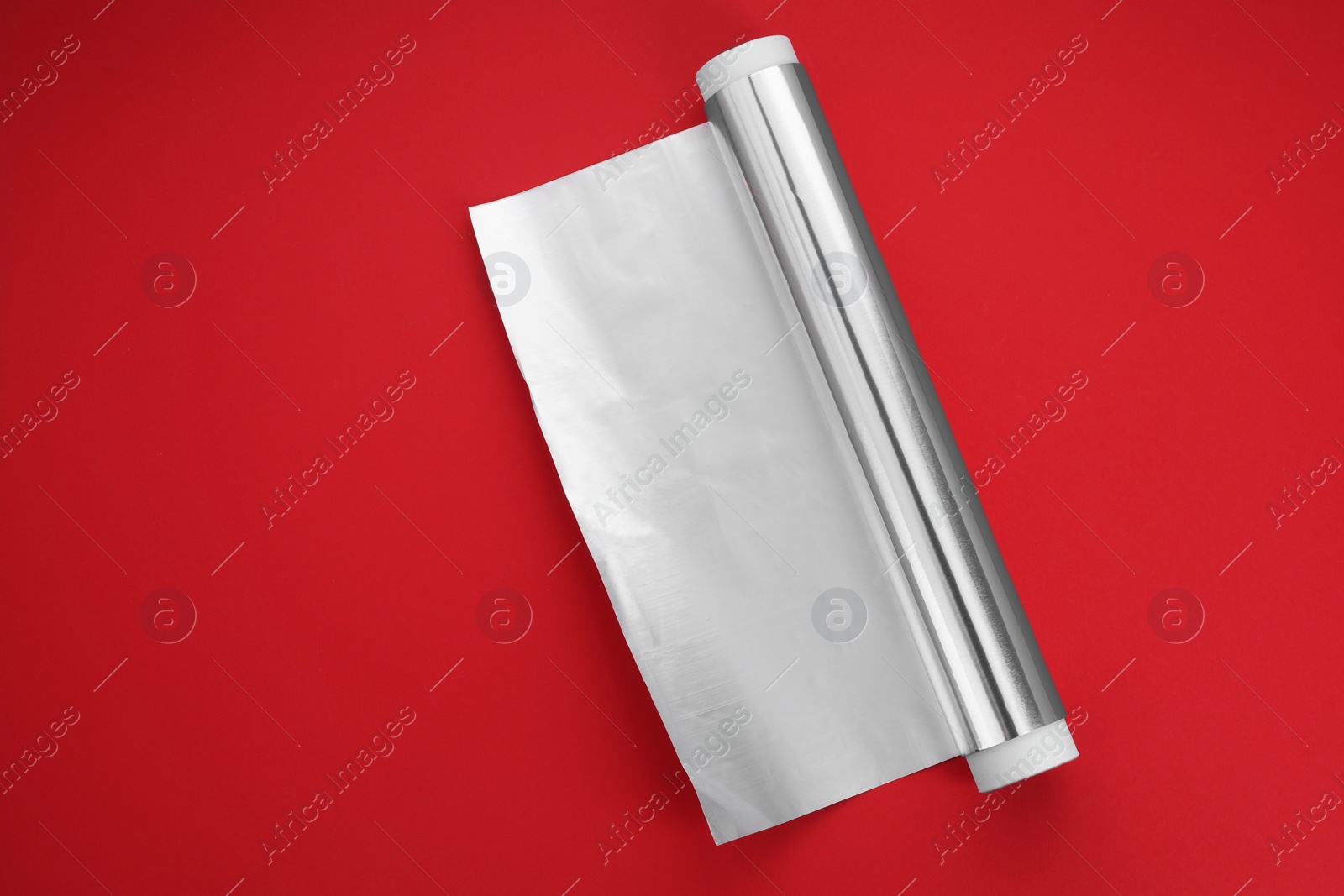 Photo of Roll of aluminum foil on red background, top view