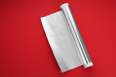 Roll of aluminum foil on red background, top view