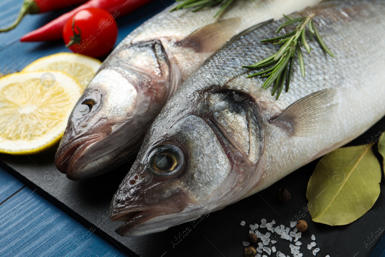 Photo of Tasty sea bass fish and ingredients on blue wooden table, closeup