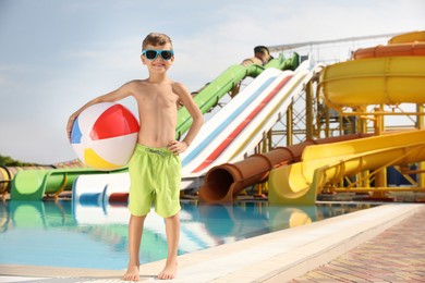Photo of Cute little boy with inflatable ball near pool in water park, space for text