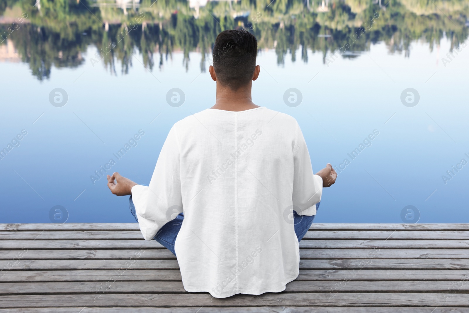 Photo of Man meditating on wooden pier near river, back view