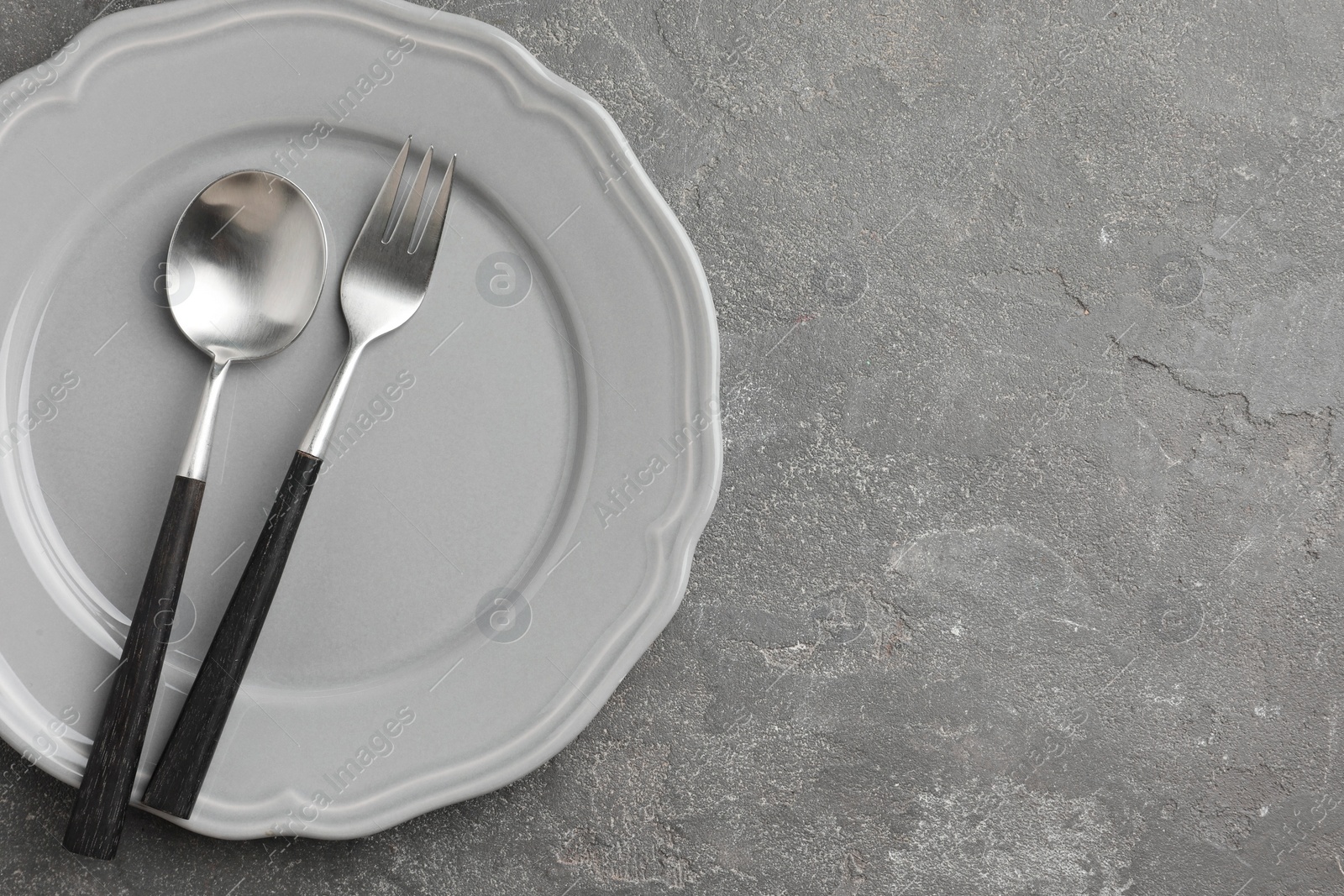 Photo of Stylish setting with cutlery and plate on grey textured table, top view. Space for text