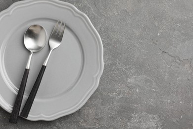 Stylish setting with cutlery and plate on grey textured table, top view. Space for text