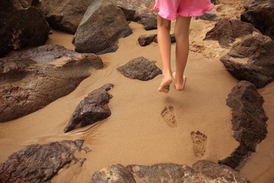 Photo of Little girl walking on sandy beach, closeup