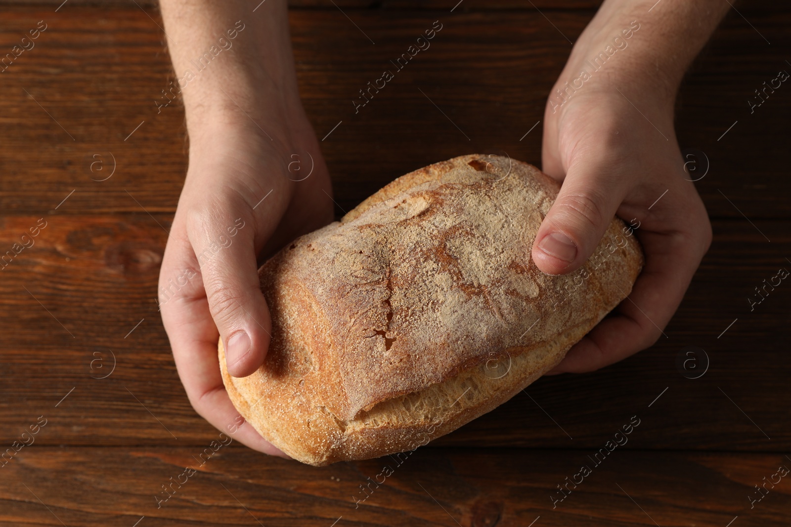 Photo of Man holding loaf of fresh bread at wooden table, top view