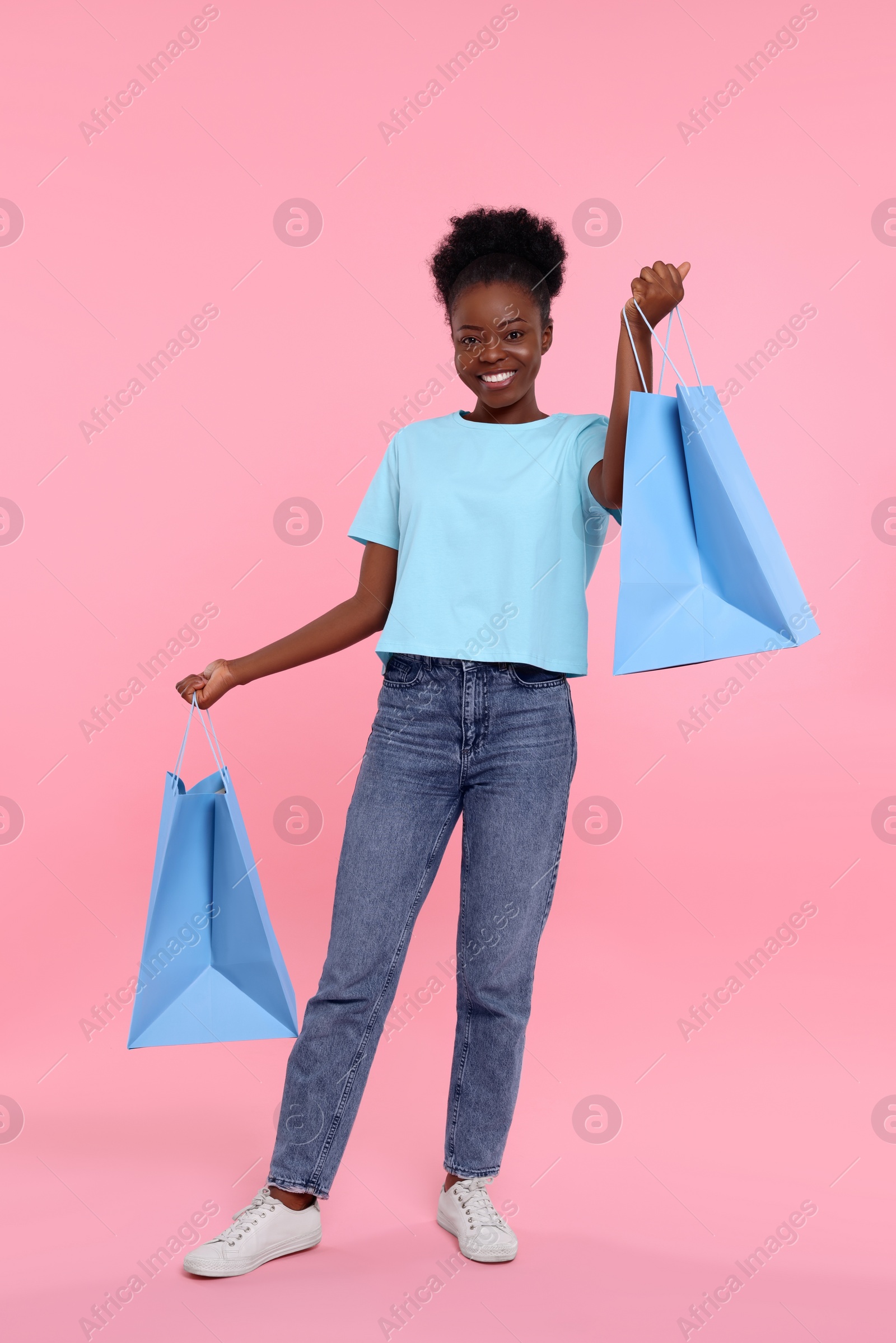 Photo of Happy young woman with shopping bags on pink background