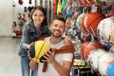 Photo of Little school girl with father choosing ball in supermarket