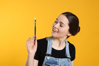 Photo of Woman with paintbrush on yellow background. Young artist