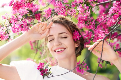 Photo of Attractive young woman posing near blossoming tree on sunny spring day