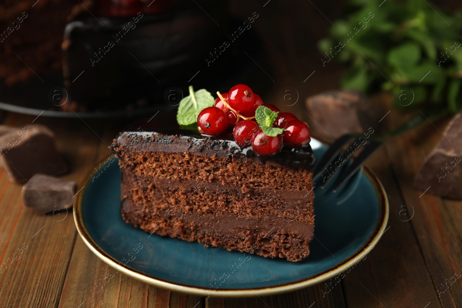 Photo of Piece of tasty homemade chocolate cake with berries and mint on wooden table