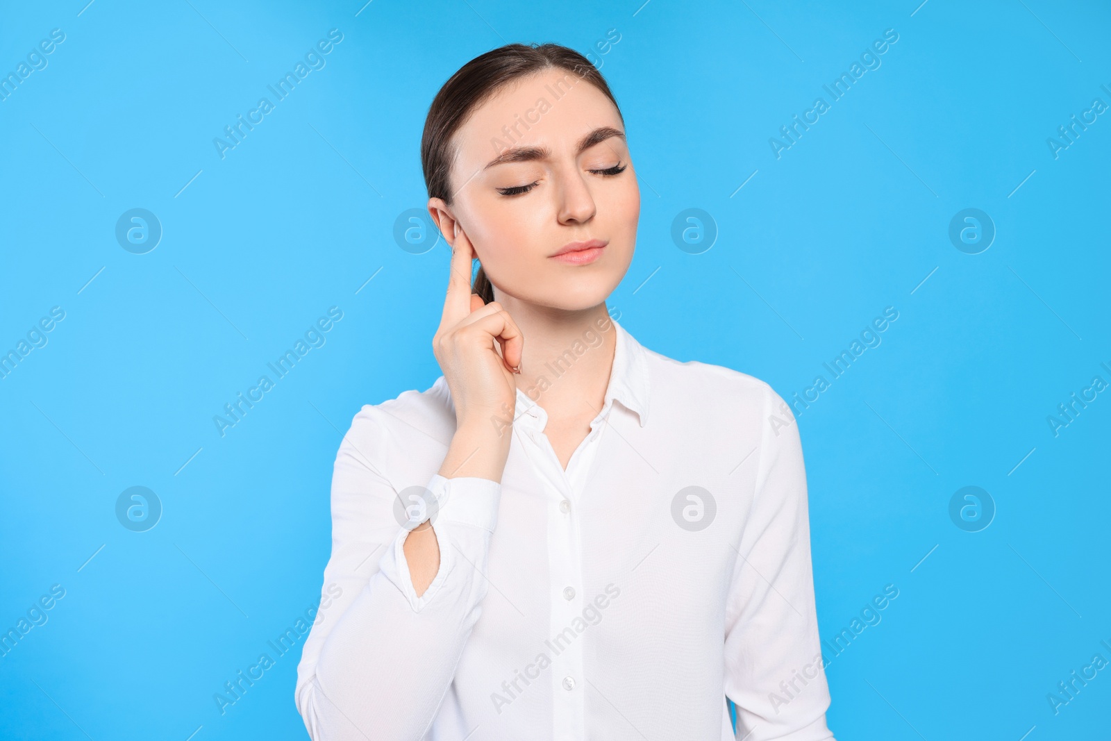 Photo of Young woman suffering from ear pain on light blue background