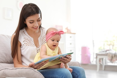 Photo of Young mother with her cute baby girl reading book in armchair at home