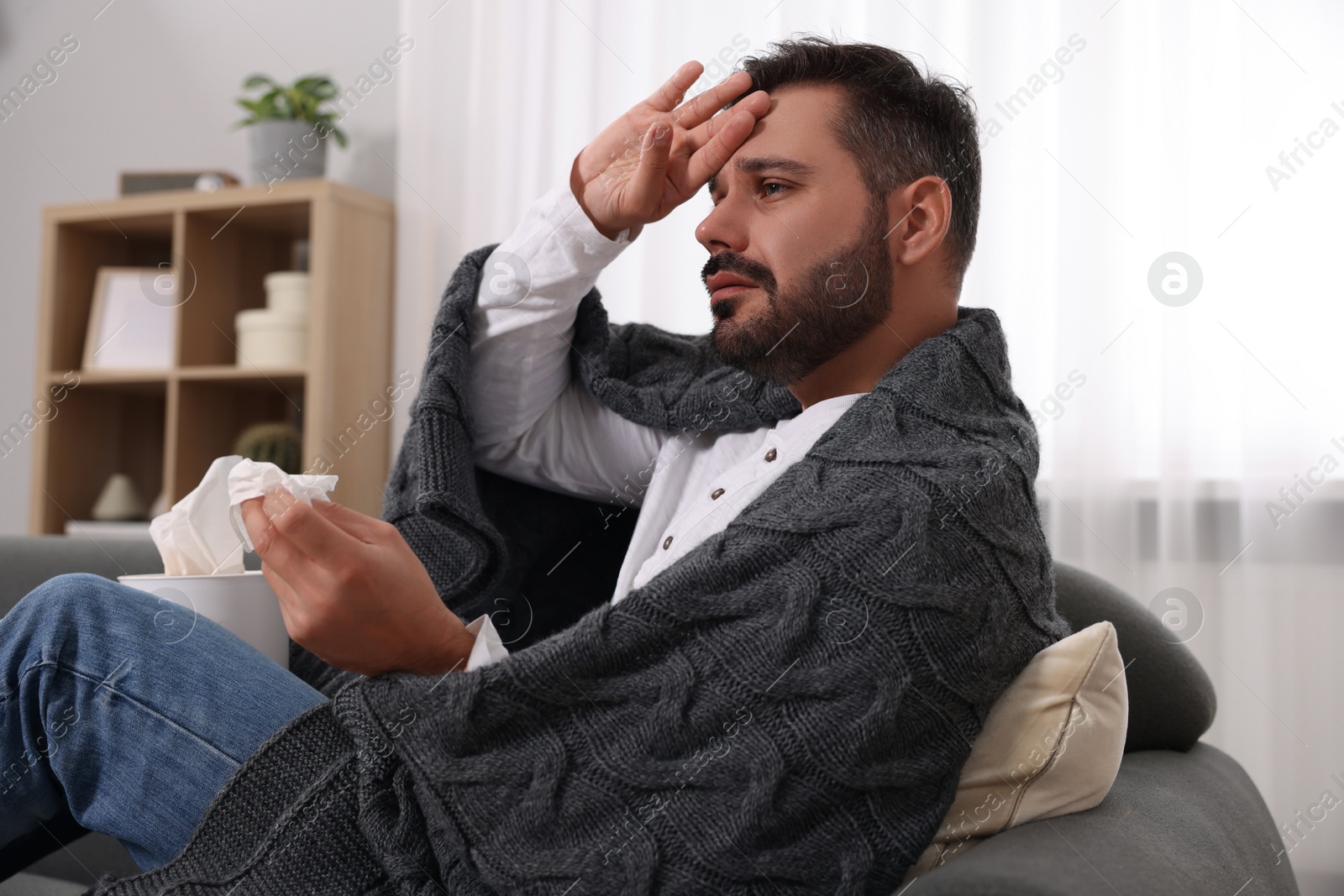 Photo of Sick man wrapped in blanket with tissue on sofa at home. Cold symptoms