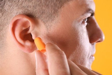 Photo of Man inserting foam ear plug on yellow background, closeup