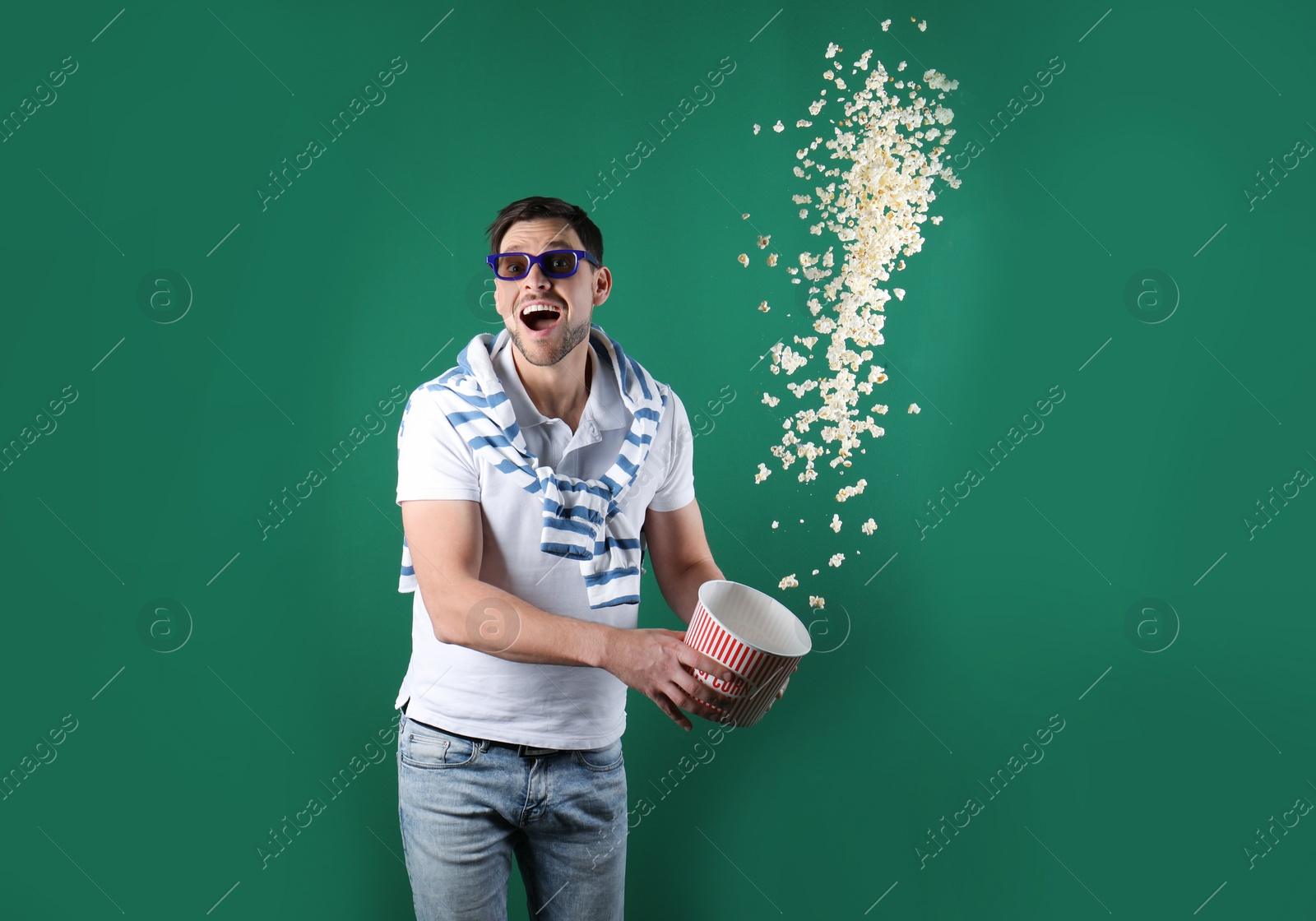 Photo of Emotional man with 3D glasses throwing popcorn on color background