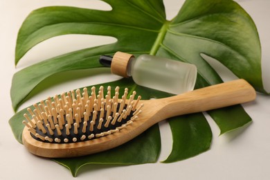 Photo of Wooden hair brush, bottle of essential oil and monstera leaf on white table