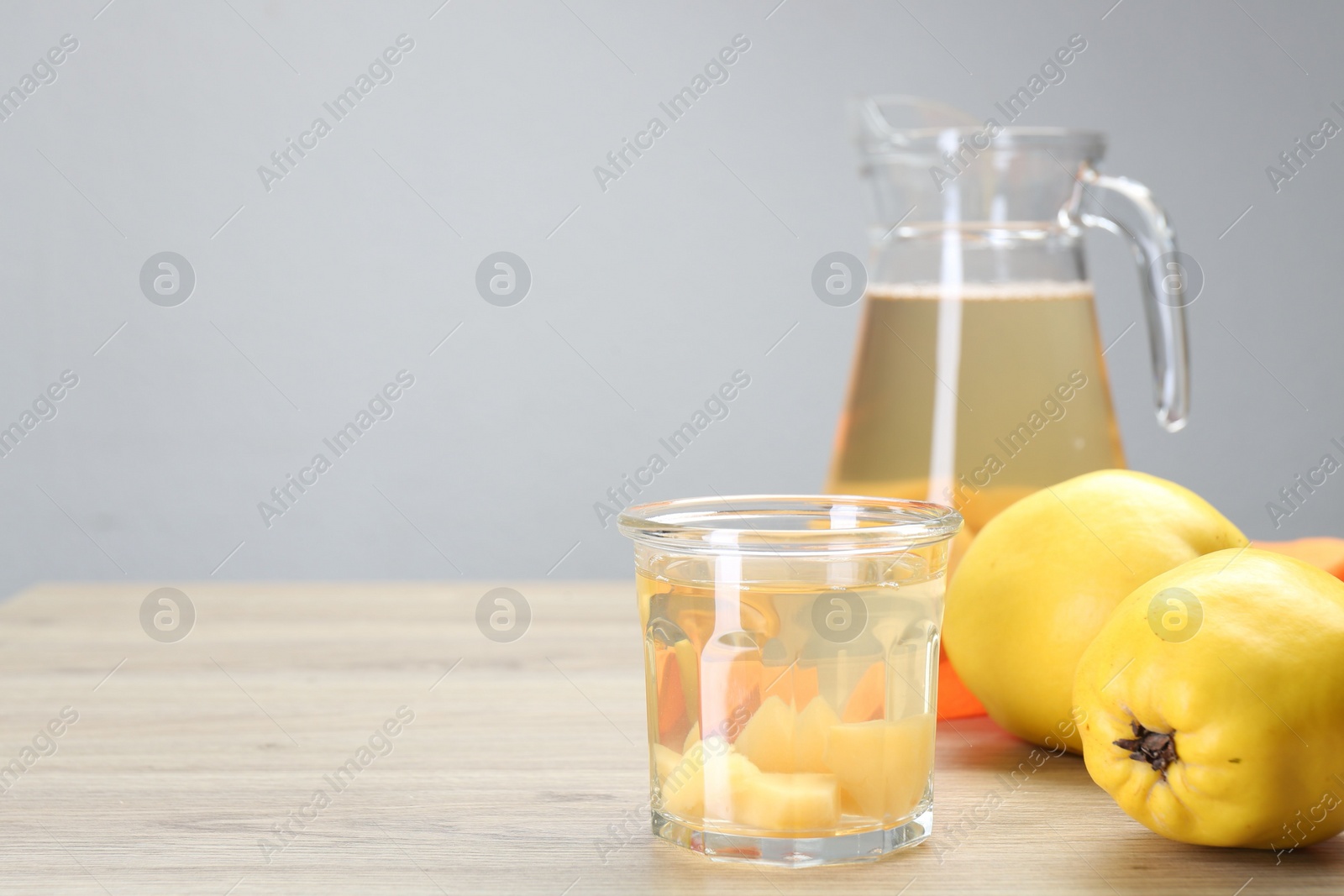 Photo of Delicious quince drink in glass and fresh fruits on wooden table, space for text